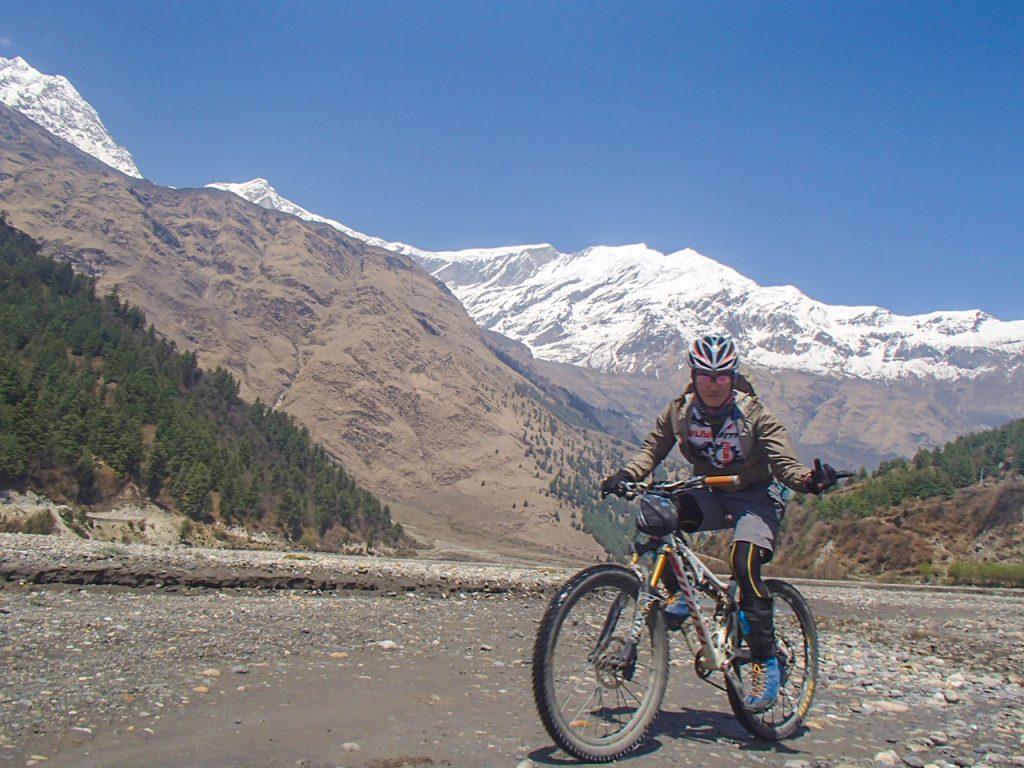 A man riding a bike along a scenic trail with the majestic mountain range in the background, surrounded by Himalayan landscape while Biking in Upper Mustang.