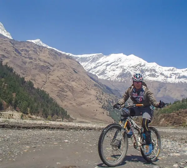 A man riding a bike along a scenic trail with the majestic mountain range in the background, surrounded by Himalayan landscape while Biking in Upper Mustang.