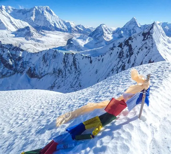 Colorful prayer flags fluttering on a mountain ridge with snow-capped peaks in the background on the Everest Base Camp trek.