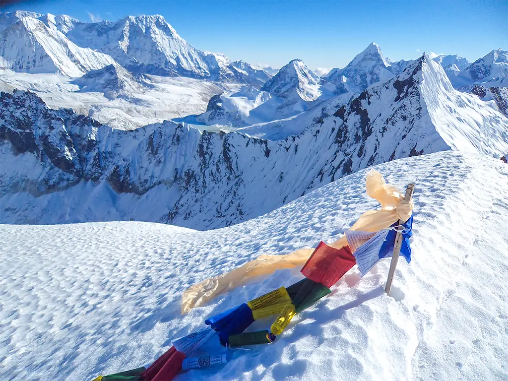 Colorful prayer flags fluttering on a mountain ridge with snow-capped peaks in the background on the Everest Base Camp trek.
