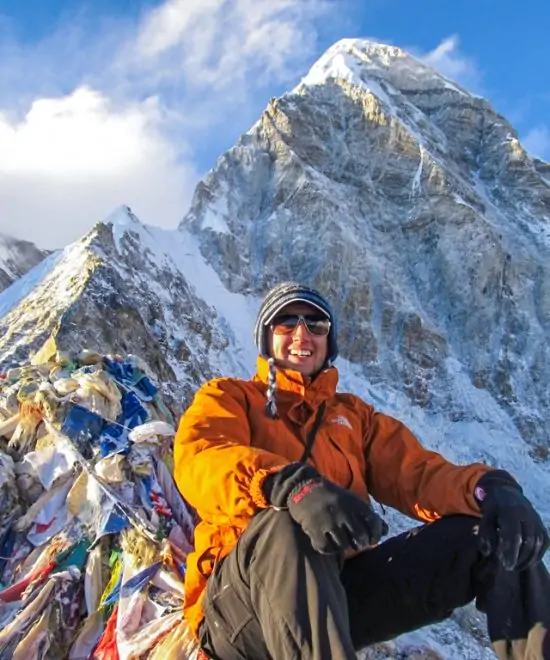 A man sitting on a rocky edge overlooking towering Himalayan mountains on the Everest Base Camp trekking trail.