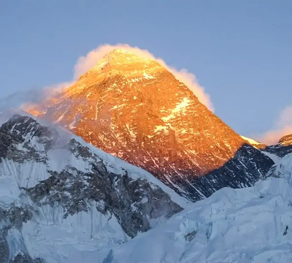 Sunlight casting a golden glow on the snow-covered summit of Mount Everest in the Himalayas during sunrise.