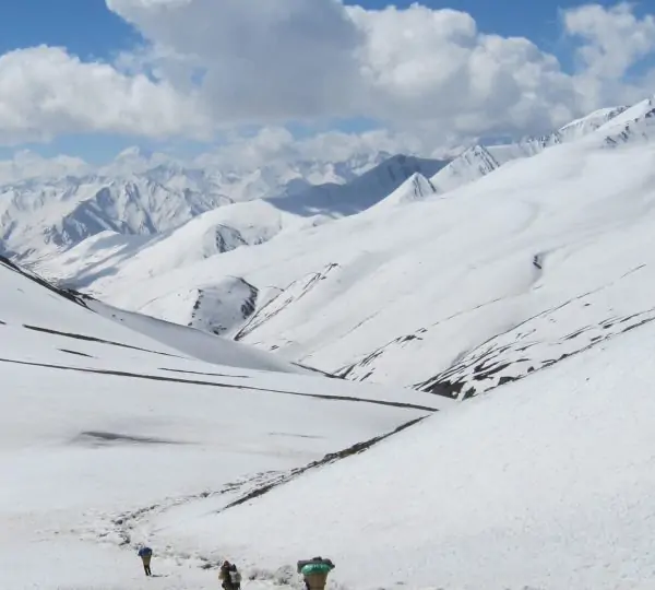 A group of trekkers walking along a trail during Pisang Peak Climbing leading toward towering snow-capped Himalayan mountains in Nepal.