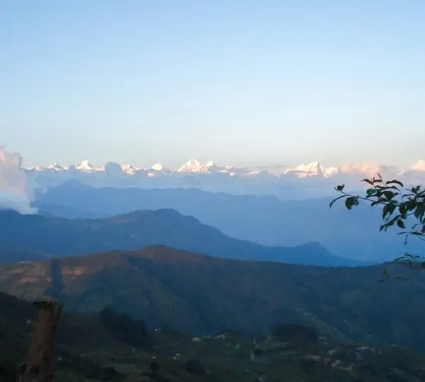 Panoramic landscape featuring green rolling hills leading up to towering snow-capped mountains under a clear sky.