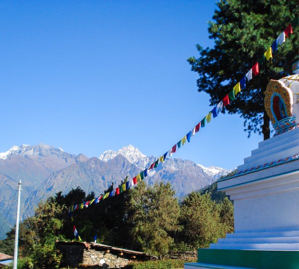 A religious landmark adorned with colorful prayer flags, set against the backdrop of snow-capped Himalayan mountains.