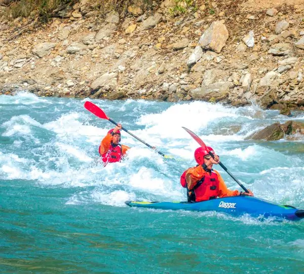 Two people paddling kayaks side by side on a flowing river surrounded by lush greenery and natural landscapes in Kayaking Courses in Nepal
