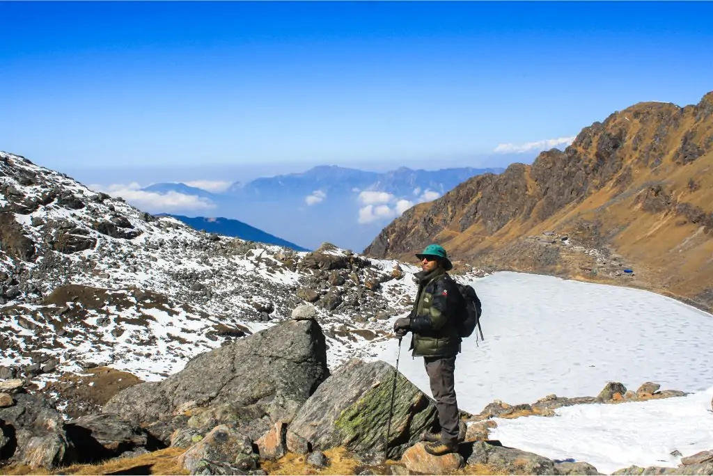 A man standing outdoors, looking forward thoughtfully, with Himalayan mountains visible in the background. Trekking in Nepal