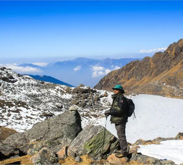 A man standing outdoors, looking forward thoughtfully, with Himalayan mountains visible in the background.