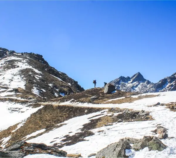 A man standing on a mountain peak in the Himalayas, quietly looking ahead with mountains in the background on route to Helambu PanchPokhari BhairabKunda Trek.