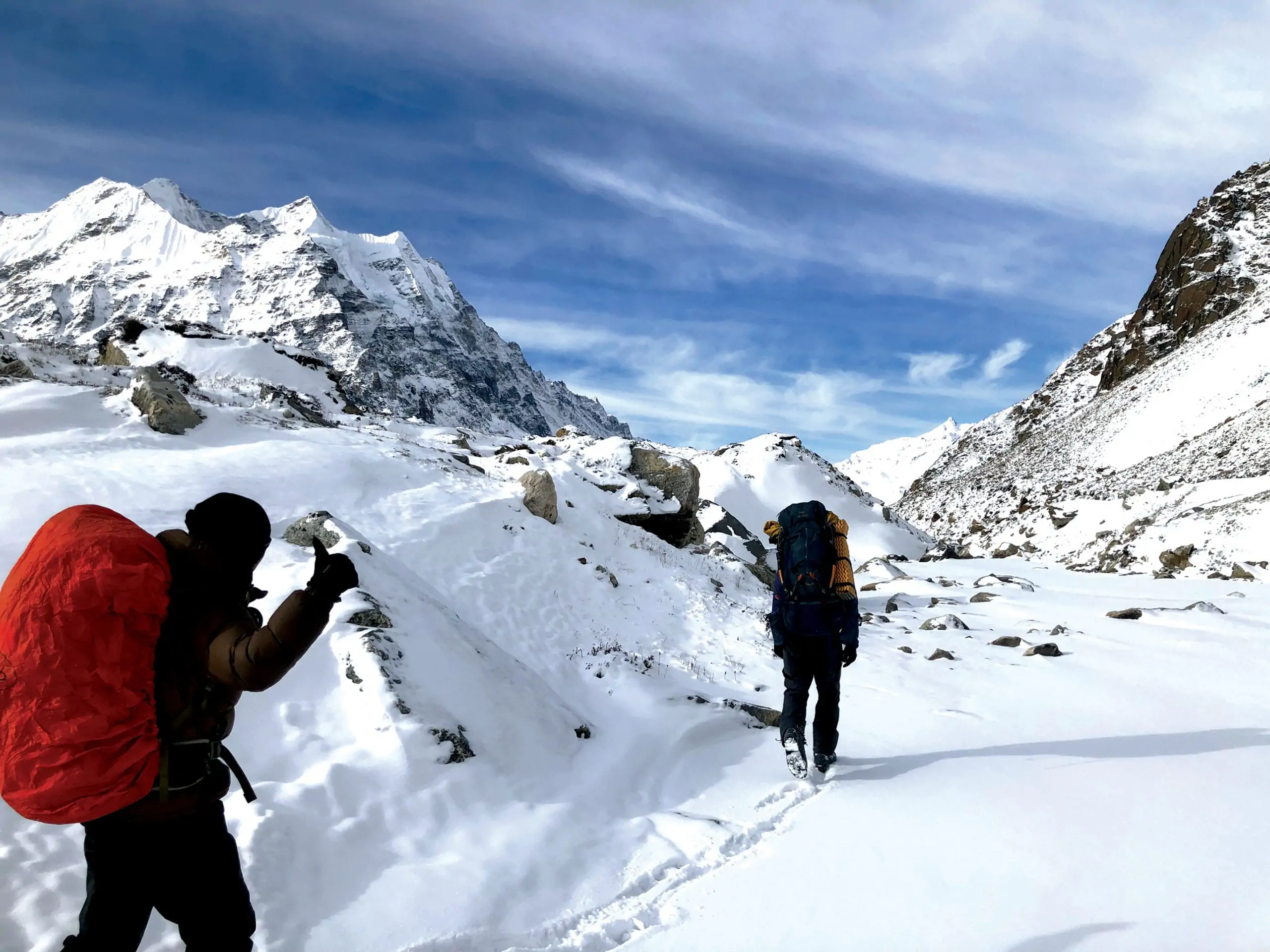 A group of trekkers walking along a rugged mountain trail surrounded by towering peaks on the way to Kanchenjunga Base Camp Trekking.