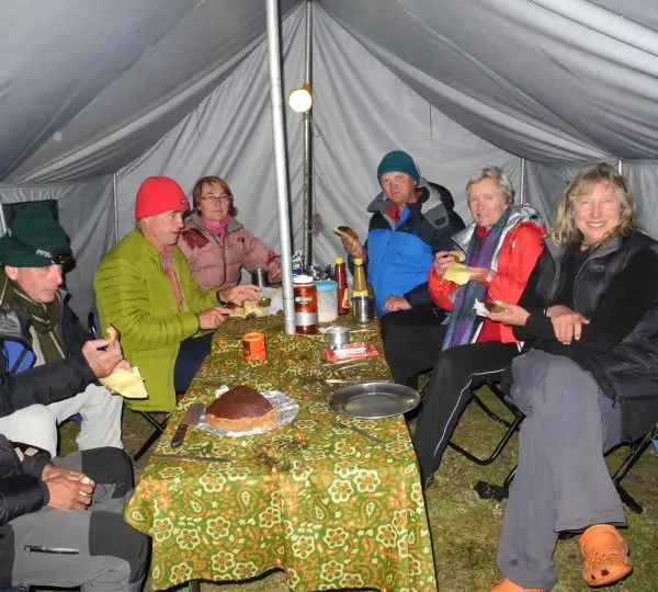 A group of tourists sitting inside a camping tent, happily sharing food and enjoying a meal during a trekking expedition in Nepal.