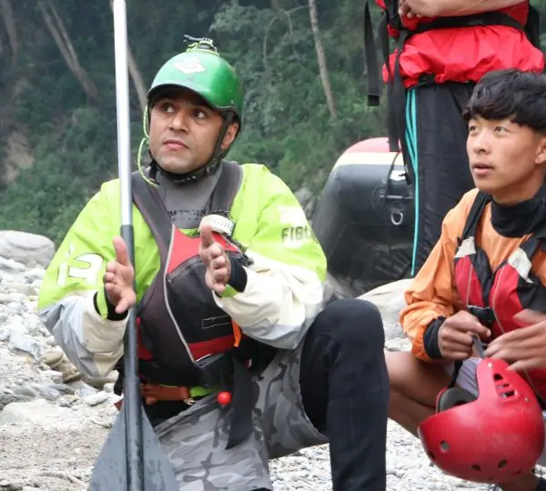 A man wearing a helmet and life jacket, holding a paddle, prepared to start rafting on a river in Nepal.
