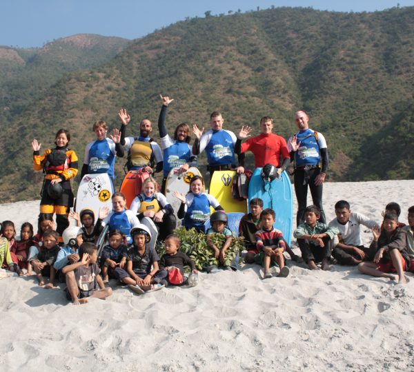 A joyful group of rafters posing together with smiles and raised paddles after completing a rafting trip on the Karnali River in Nepal.