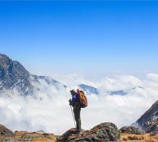 A man seen from behind standing on a mountain ledge with clouds blanketing the valley below during everest base camp trek.