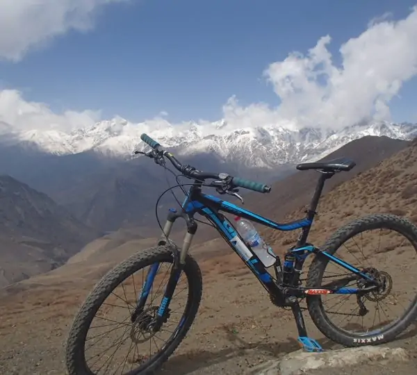 A bike parked on a route in Bike Annapurna Round with the snow-covered mountain range in the background under a clear blue sky.