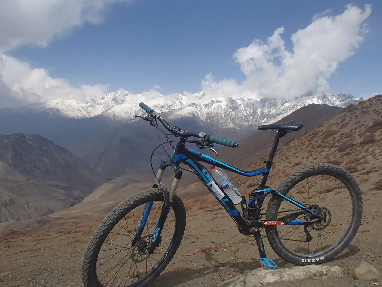 A bike parked on a route in Bike Annapurna Round with the snow-covered mountain range in the background under a clear blue sky.