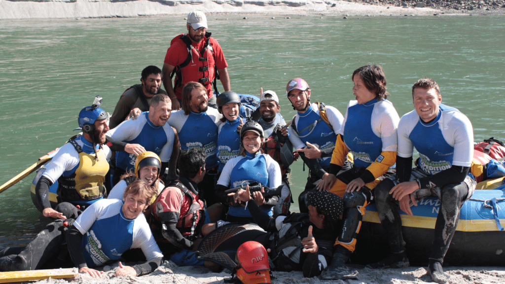 Group of smiling tourists posing with raised paddles after completing a thrilling rafting trip on a river in Nepal.
