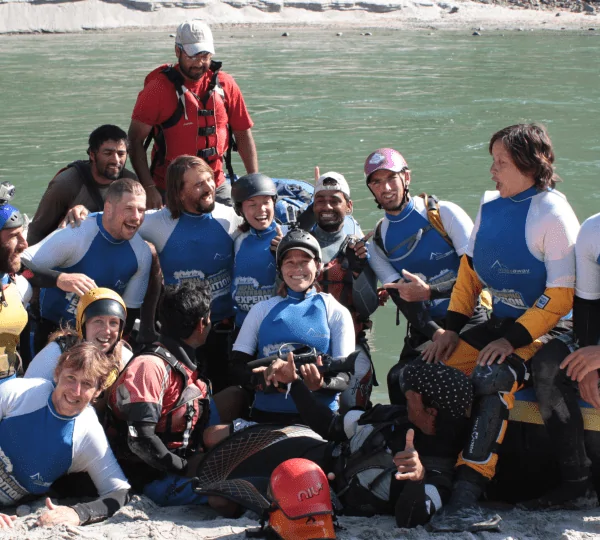 Group of smiling tourists posing with raised paddles after completing a thrilling rafting trip on a river in Nepal.