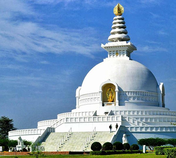 The white-domed Peace Stupa standing atop a hill, overlooking lush landscapes with the Himalayas in the distance.