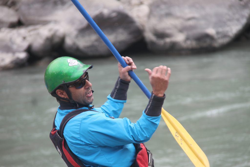 A man wearing a helmet and life jacket, rafting through the rapids of the Karnali River in Nepal.