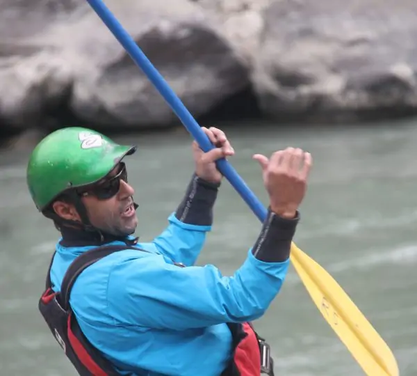 A man wearing a helmet and life jacket, guiding how to raft through the rapids of the Karnali River in Nepal.