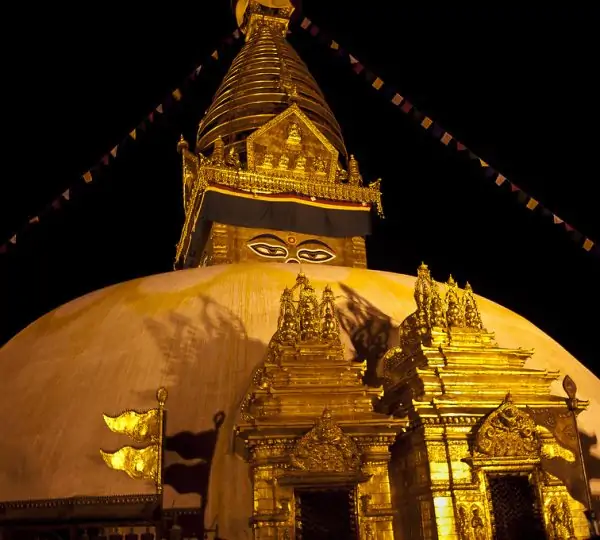 Swayambhunath Stupa glowing under night lights in Kathmandu, Nepal, with golden spire and prayer flags softly lit against the dark sky.