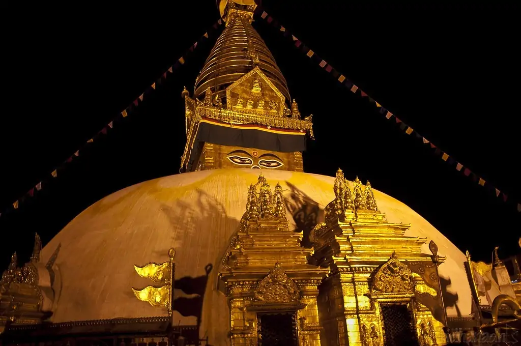 Swayambhunath Stupa glowing under night lights in Kathmandu, Nepal, with golden spire and prayer flags softly lit against the dark sky.
